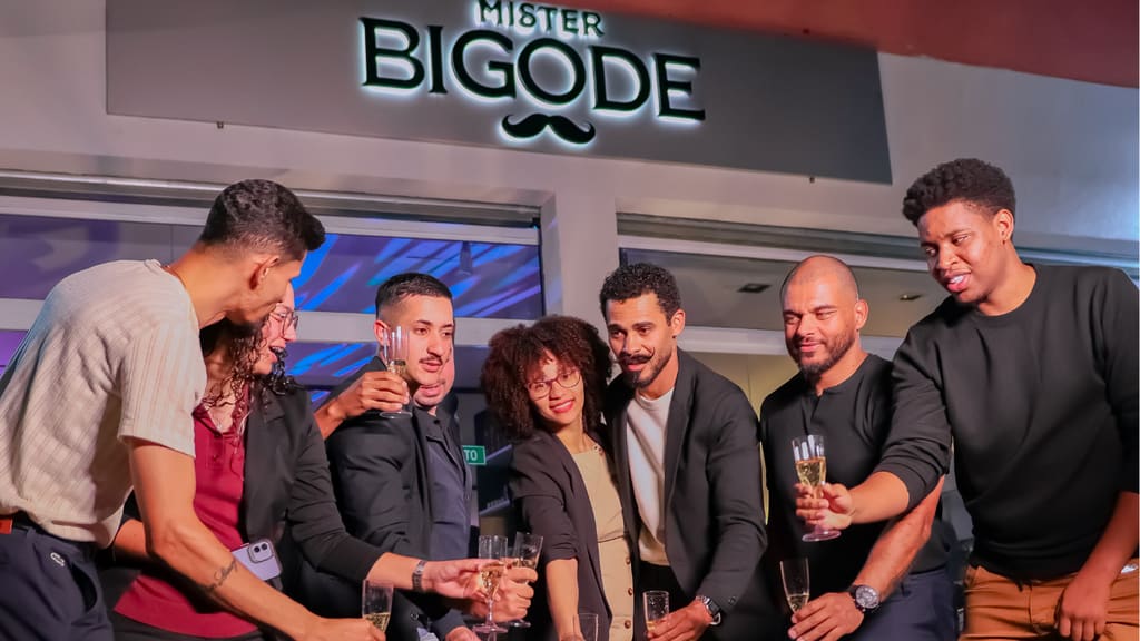 Equipe da Mister Bigode brindando sob o letreiro da barbearia